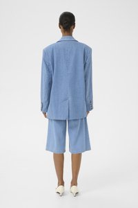 Light blue denim blazer with loose fit, single vent, and button accents, paired with matching knee-length shorts. Smooth texture.