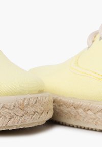Espadrilles en toile jaune avec semelles en jute, présentant des coutures visibles et un design à bout rond, exposées côte à côte.