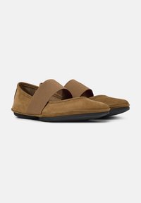 Zapatos de ante marrón con un acabado suave, que presentan bandas elásticas anchas en la parte superior y una suela flexible de goma negra.