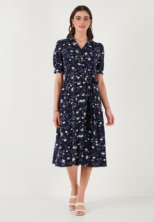 Navy floral midi dress with short puff sleeves, a collared neckline, tie waist, and mixed white and yellow flower patterns throughout.