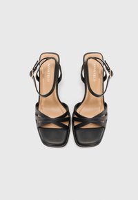 Schwarze Absatzsandalen mit quadratischer Zehenpartie, schlanken, überkreuzten Riemen und einem verstellbaren Knöchelriemen. Glattes Leder mit einer beigen Innensohle.