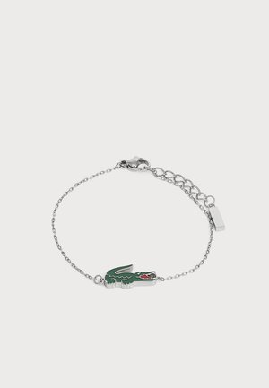 Bracelet chaîne en argent avec un pendentif crocodile vert et rouge et une fermeture réglable sur un fond clair uni.