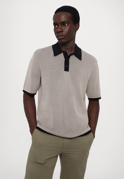 Polo à manches courtes en tissu côtelé beige clair avec un col noir et des bordures noires, doté d'un plastron à boutons.