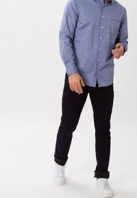 Blå knapp-up skjorta med bröstficka, i kombination med svarta byxor och vita sneakers. Skjortan har en texturerad tyg och en slim fit-design.