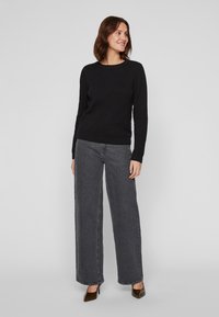 Μαύρος υφασμάτινος σκούφος με στρογγυλή λαιμόκοψη, συνδυασμένος με ψηλές γκρι τζιν παντελόνες σε ίσια γραμμή και καφέ μυτερές γόβες. Απλός και διακριτικός σχεδιασμός.