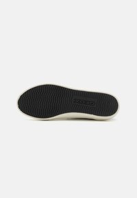 Black rubber shoe sole with textured wavy pattern, bordered by a cream-colored edge. Features "GEOX" logo in the center.