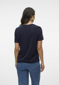 Mörkblå kortärmad T-shirt med rund halsringning, i mjukt bomullsmaterial, stylad med högmidjade jeans i denim, med detaljer på ryggen och guldörhängen.