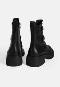 Bottes chelsea en cuir noir avec une semelle épaisse, dotées de deux boucles latérales, d'une fermeture éclair et d'une texture lisse.