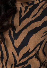 Maglione marrone con un motivo a righe di tigre nero. Il materiale sembra morbido e strutturato, con scollatura a girocollo e maniche lunghe.