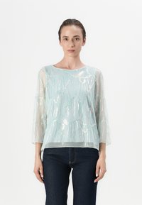 Blusa leggera azzurro chiaro con intricate ricami in argento e maniche a tre quarti, presenta un colletto rotondo e un design fluido.
