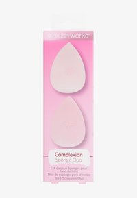 Zwei pinke, tropfenförmige Makeup-Schwämme in einer Verpackung. Die Schwämme haben eine glatte Textur und ein kleines geprägtes Sternenmotiv oben. 