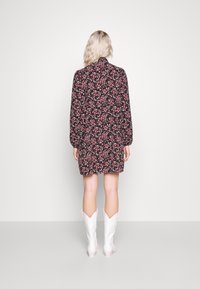 Schwarzes Blumenkleid mit kleinen pinken und weißen Blumen, langen Ärmeln und hohem Kragen. Getragen mit weißen Cowboystiefeln.