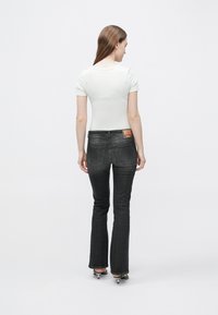 Λευκό τοπ με κοντά μανίκια σε συνδυασμό με σκούρο γκρι τζιν με φαρδιά άκρα, που διαθέτει κλασικό σχέδιο με πέντε τσέπες και πατς με λογότυπο στη ζώνη πίσω.