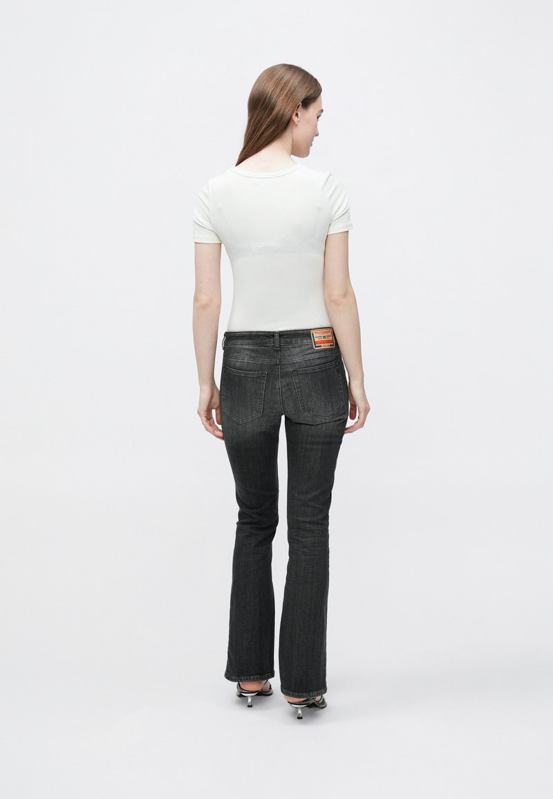 Witte top met korte mouwen gecombineerd met donkergrijze, uitlopende jeans met een klassieke vijfzakkenontwerp en een logopatch op de achterkant van de tailleband.