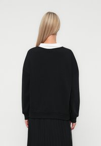 Svart hettegenser med hvit krage, med lange ermer og en avslappet passform. Stoffet ser mykt ut med en jevn tekstur.