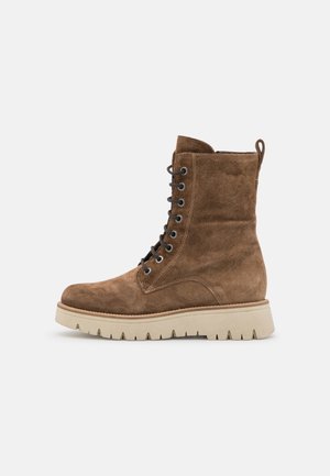 Brauner Wildleder-Stiefelette mit Schnürung, dicker beiger Profilsohle und Zuglasche hinten, von der Außenseite gezeigt.