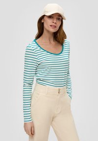 Langarmshirt mit türkis und weißen horizontalen Streifen, Rundhalsausschnitt. Kombiniert mit beigen, hochgeschnittenen Hosen. Hellfarbige Kappe.