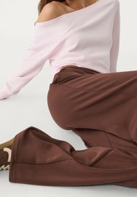 Hellrosa schulterfreies Sweatshirt kombiniert mit locker sitzenden, rostbraunen Hosen mit weitem Bein. Weiche Textur und minimalistisches Design mit einem lässigen Look.