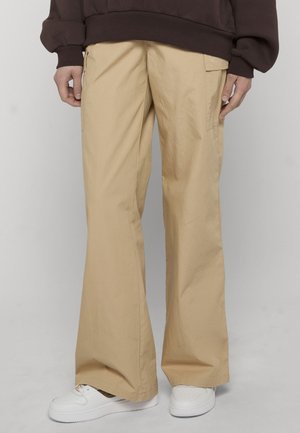 Beige wide-leg pants with side pockets worn with white sneakers and a dark brown oversized sweatshirt on a standing person.