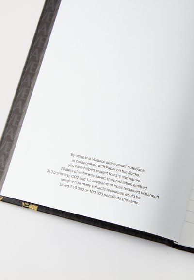 Notebook Versace in carta stone con copertina nera testurizzata e motivo dorato. Include pagine bianche con informazioni ecologiche stampate all'interno.