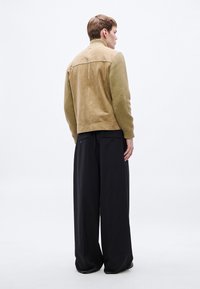 Tpruun nahast jakk soonikkoes varrukate, kõrge krae ja siledapinna ning lahtiste mustade pükstega, mille külgedel on taskud.