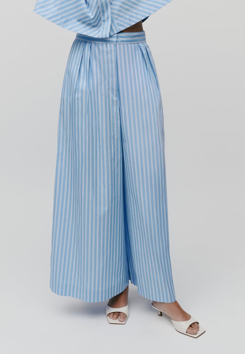 Lichtblauwe gestreepte wijde broek van satijn. Heeft plooien, een hoge taille en een contrasterende tailleband. Gecombineerd met witte open teen hakken.