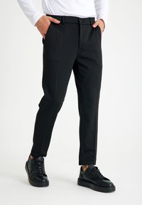 Zwarte op maat gemaakte broeken met een gladde textuur, zijzakken en een knoopsluiting. Draag ze met zwarte sneakers met gestructureerde accenten.