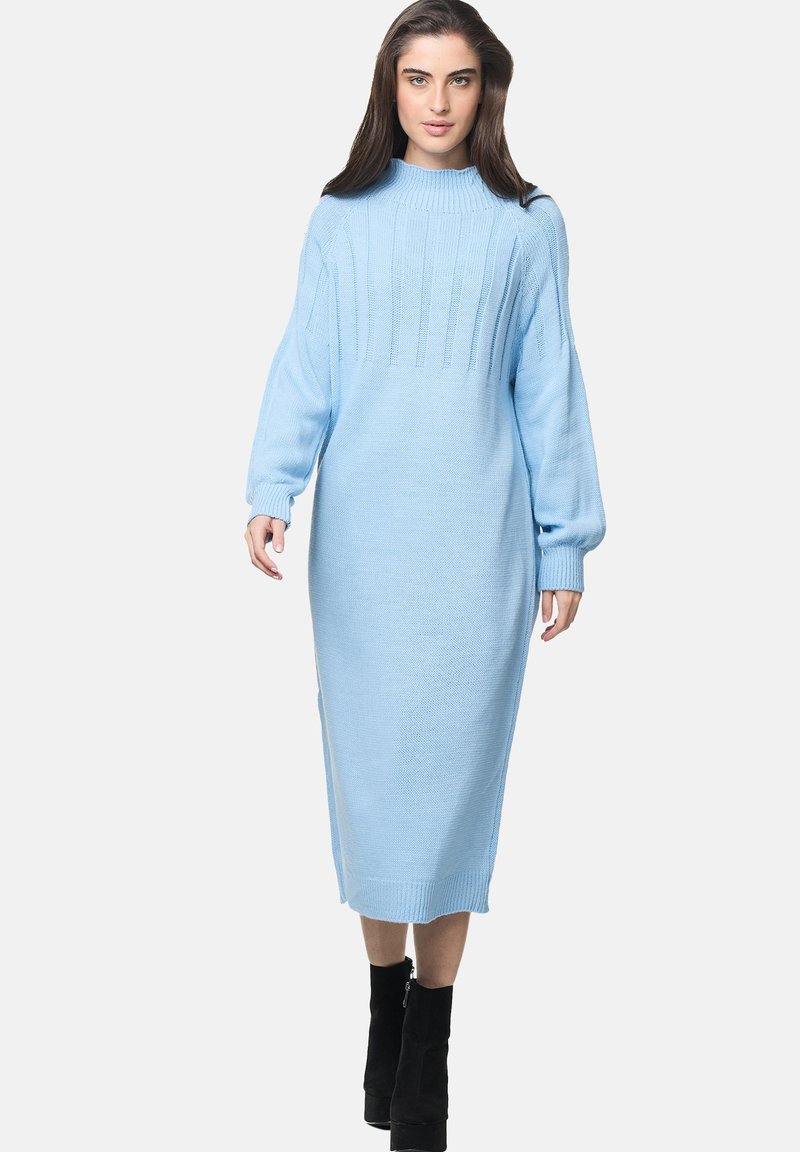 Abito maglione midi di colore azzurro chiaro, lavorato a maglia con texture a coste, maniche a palloncino lunghe e fessure laterali, abbinato a stivaletti neri alla caviglia.
