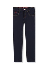Jean bleu foncé avec une coupe slim, présentant des coutures jaunes, cinq poches et un petit logo rouge sur le devant. Texture denim lisse.