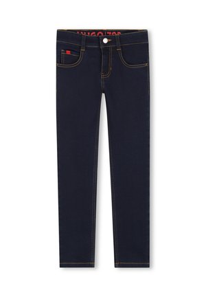 Temno modri kavbojki z ozko prilegajočim krojem, z rumenim šivom, petimi žepi in majhnim rdečim logotipom spredaj. Gladka denim tekstura.