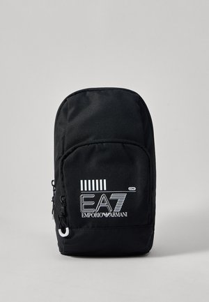 Sac à dos en nylon noir avec une forme arrondie. Comprend une poche avant zippée, un logo blanc et des rayures verticales sur le panneau supérieur.