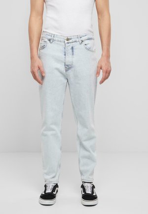 Light blue denim jeans feature five pockets, a button closure, and visible stitching details. Worn with black and white sneakers.