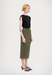 Mustat lyhythihaiset paitatopit yhdistettyinä viininpunaisen draperoidun midi-hameen kanssa. Mallilla on päällä mustat nauhaketjut korkokengät. Silkkiset kankaat ja istuva malli.