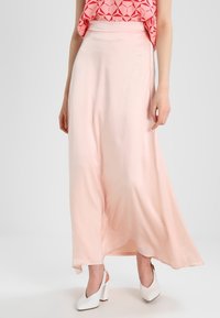 Lång, flödande rosa kjol i smidig tyg, med hög midja och en något utsvängd fåll. Bärs med vita klackskor.