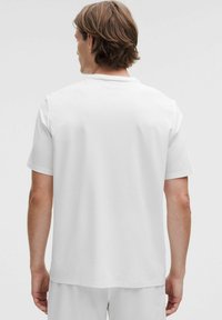 Camisa blanca de manga corta con textura acanalada, cuello redondo y dobladillo recto, vista desde la parte trasera. Diseño minimalista.