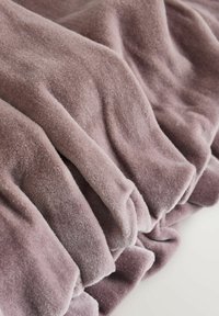 Weiche, strukturierte Decke in hellem Mauve, mit Falten und einem plüschigen Finish. Sichtbare Fasern betonen ihr gemütliches Aussehen.