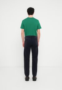  Πράσινο βαμβακερό t-shirt με κοντά μανίκια συνδυασμένο με σκούρο τζιν παντελόνι. Η εμφάνιση ολοκληρώνεται με μαύρα παπούτσια και απαλή υφή.