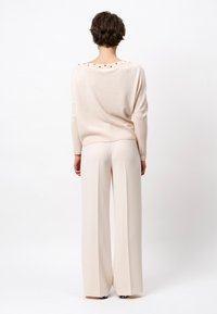 Lichtbeige sweater met een ruime halslijn, voorzien van decoratieve knopen op de achterkant. Gecombineerd met loszittende, crèmekleurige high-waisted broeken.