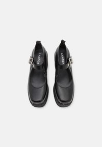 Black leather Mary Jane shoes with a square toe, adjustable buckle strap, and textured black sole. Interior features a smooth finish.