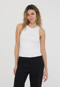 Top bianco senza maniche con scollatura rotonda, caratterizzato da un motivo texturizzato di piccoli punti. Abbinato a pantaloni neri a gamba dritta.