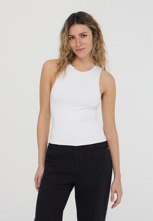 Top bianco senza maniche con scollatura rotonda, caratterizzato da un motivo texturizzato di piccoli punti. Abbinato a pantaloni neri a gamba dritta.