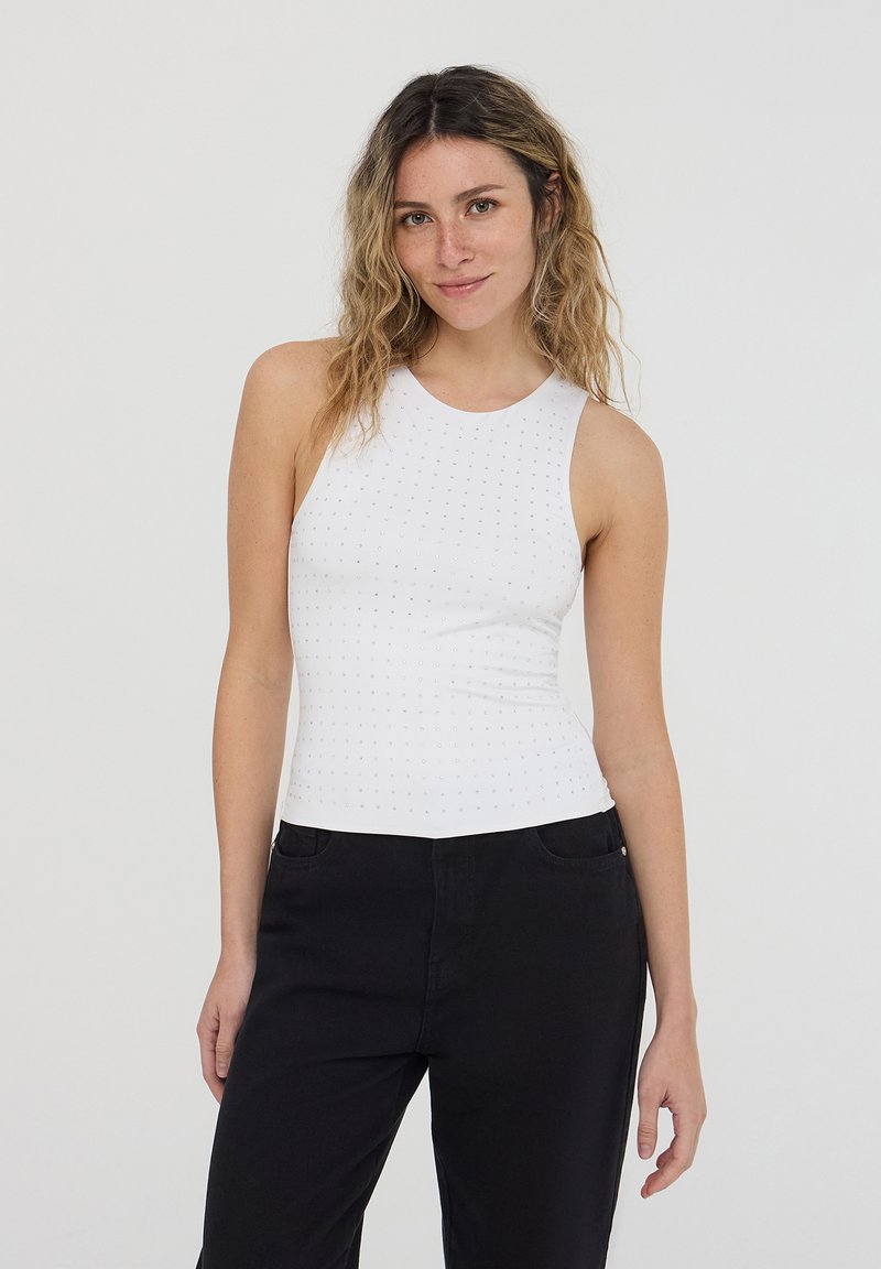 Top bianco senza maniche con scollatura rotonda, caratterizzato da un motivo texturizzato di piccoli punti. Abbinato a pantaloni neri a gamba dritta.