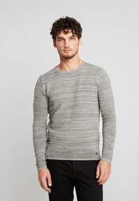 Gray long-sleeve sweater with horizontal ribbed texture, round neckline, and fitted design. Black pants are worn underneath.