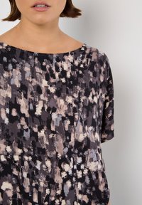 Lässige Bluse mit Rundhalsausschnitt, bestehend aus einem schwarzen Hintergrund mit abstrakten Mustern in Hellgrau, Beige und Weiß. Kurze Ärmel.