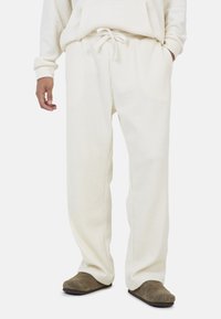 Kremowe prążkowane spodnie z elastycznym pasem i sznurkiem. Materiał ma miękką teksturę. W zestawie z brązowymi butami wsuwanymi.