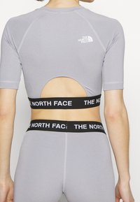 Persona que lleva un conjunto atlético de color púrpura claro con mangas cortas y espalda cortada, presentando bandas elásticas negras con el logo blanco "The North Face".