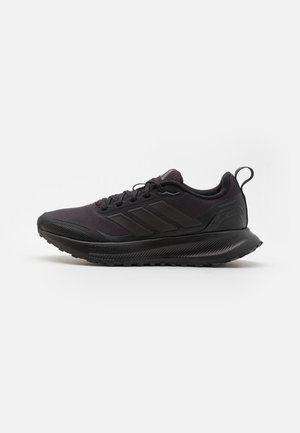 Scarpa da allenamento nera con una parte superiore testurizzata, tre strisce sui lati e una suola in gomma con un battistrada a motivo per una maggiore aderenza.