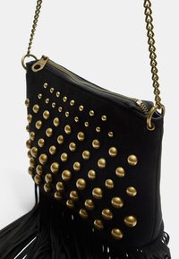 Borsa a tracolla nera in tessuto con borchie dorate, chiusura con zip e tracolla a catena; presenta dettagli in frange nella parte inferiore.