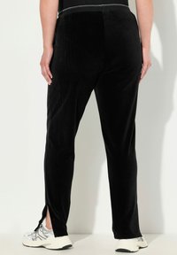 Zwarte veloursbroek met zijsplitsen, een slim fit en een elastische tailleband, gecombineerd met witte sportschoenen. Glad textuur.