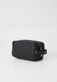 Μαύρο ορθογώνιο νεσεσέρ κατασκευασμένο από λείο ύφασμα. Διαθέτει διπλά φερμουάρ, χειρολαβή στο πλάι και καθαρό, μινιμαλιστικό σχέδιο.